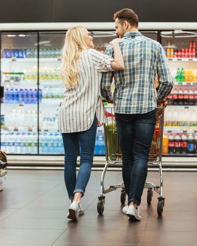 Back view of a smiling couple walking with a trolley at the supermarket